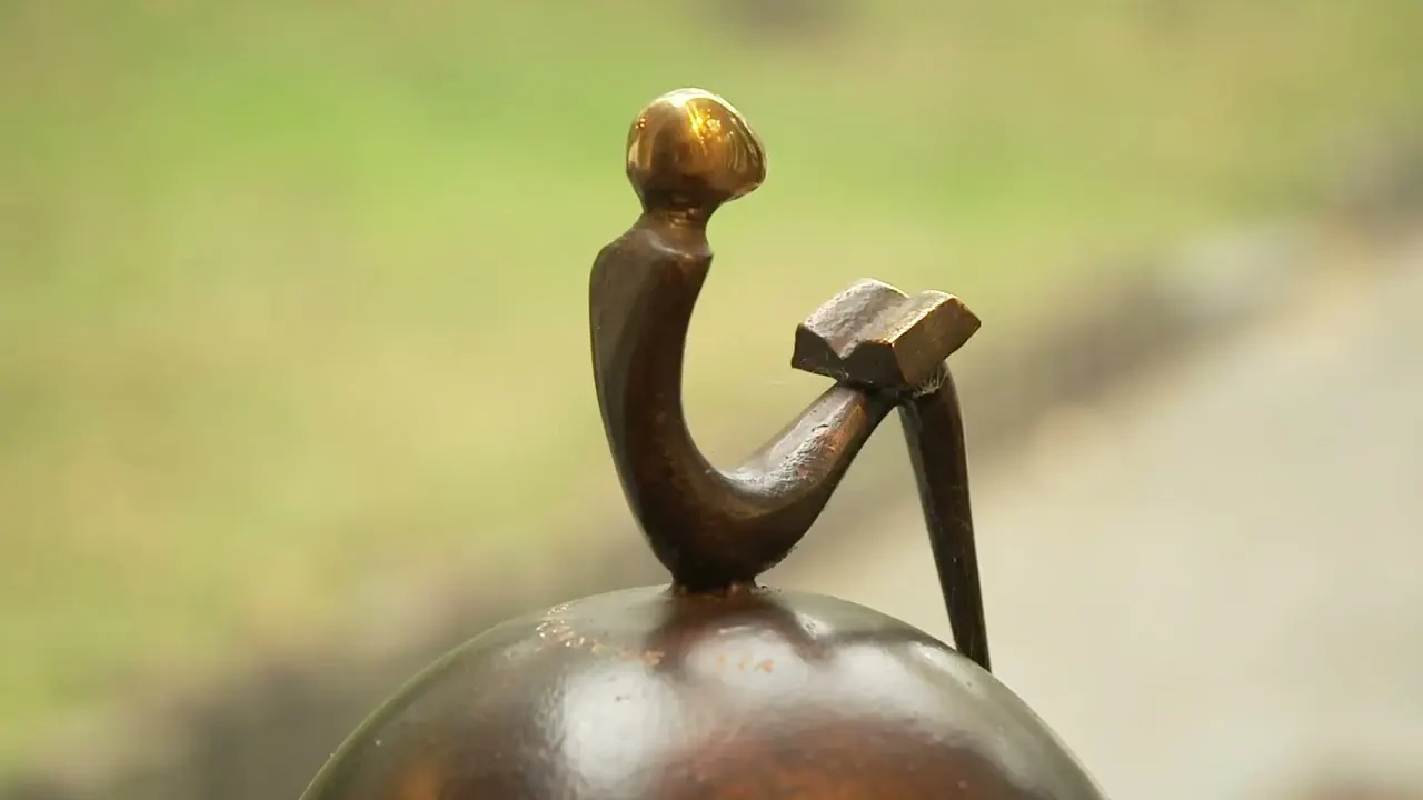 Close-up van een lezende bronzen figuur met gepolijst hoofd, uit de reportage van Kanaal Z.